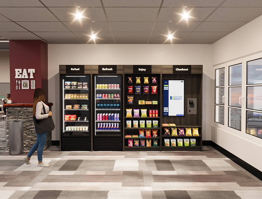 A woman stands near a self-service micro-market with snack displays, a checkout kiosk, and a sign reading "EAT" on the wall.