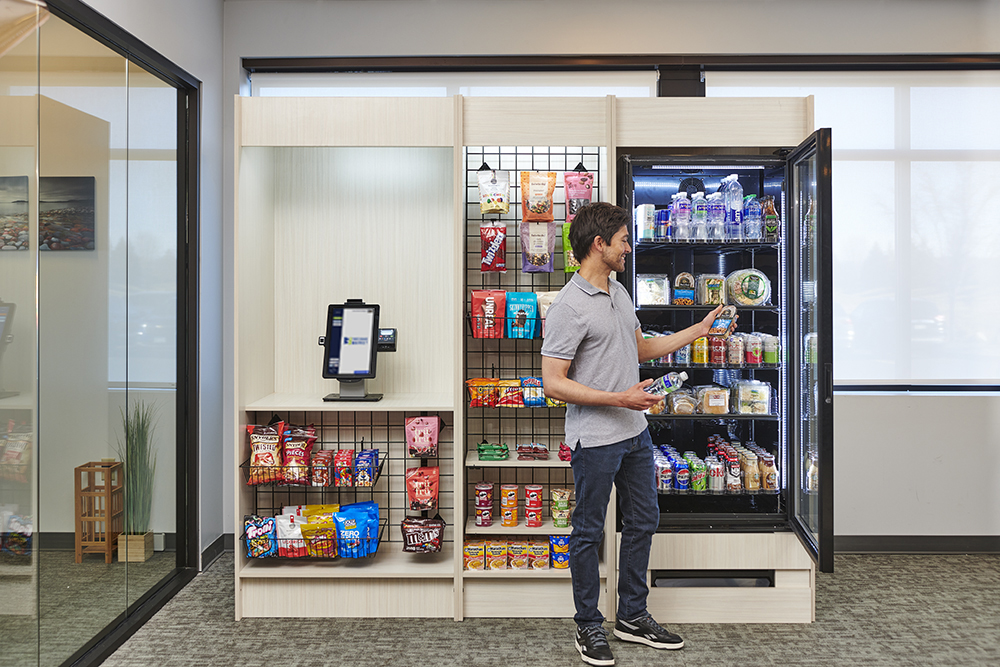 SmallMM-Go MiniX-2676 web Man browsing snacks and drinks in a modern office micro market with digital payment kiosk and refrigerated section.